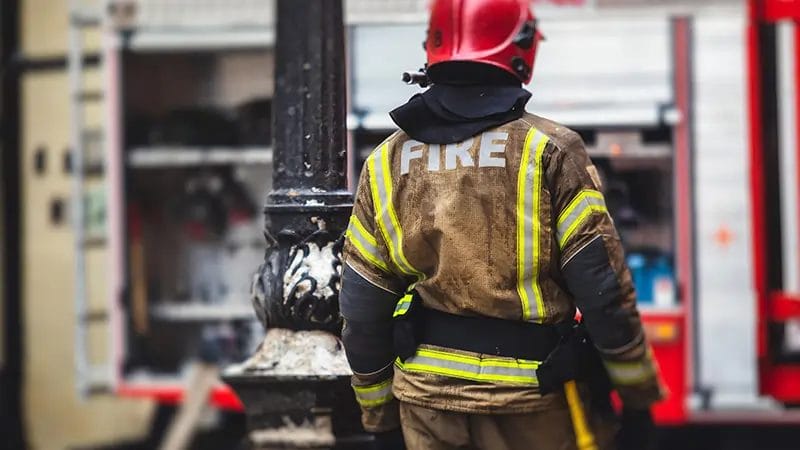 the back of a firefighter shown in full protective gear and 'FIRE' on the back of their jacket