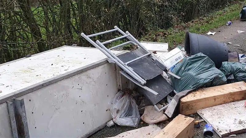 electrical items, furniture and rubbish dumped at the side of a countryside road