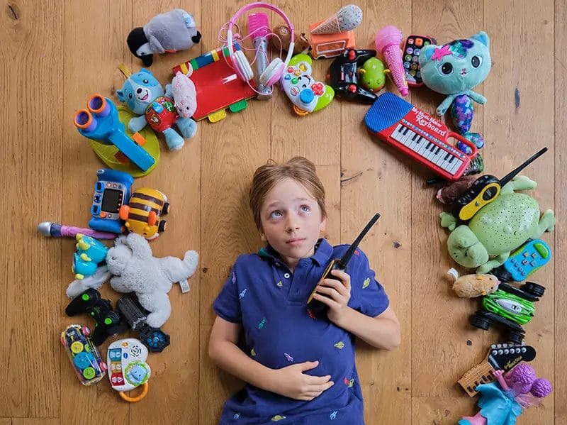 a light skinned child lying on his back with lots of toys spread in a semi circle around his head