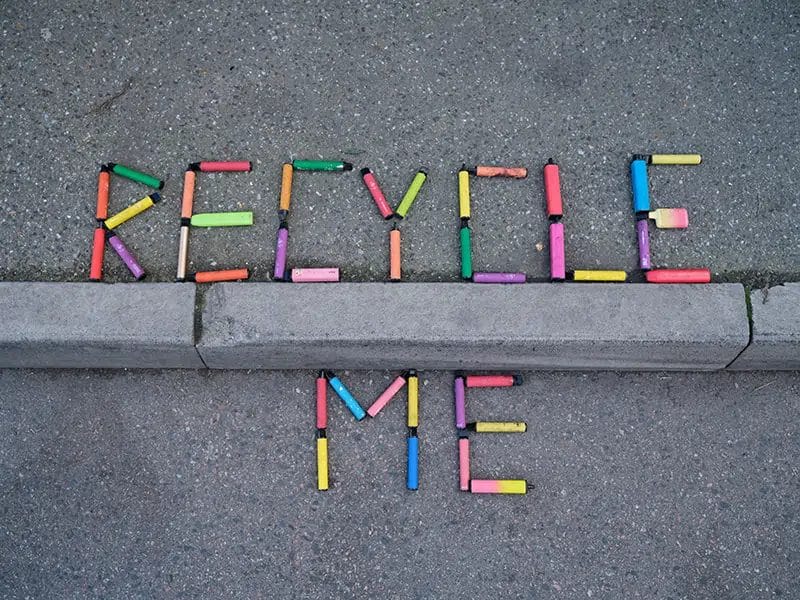 the words 'RECYCLE ME' spelt out in multi-coloured vapes on the side of a road