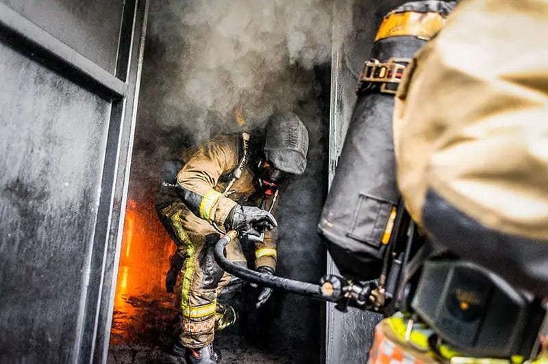 a fireman in a protective outfit emerging from a burning building with smoke pouring out around them