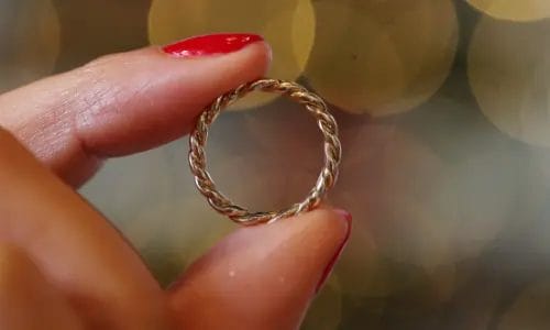 close up of light skinned woman's fingers holding a gold ring