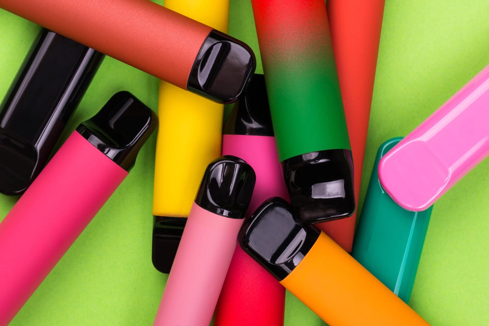 Close up of colourful vapes scattered on a bright green background.