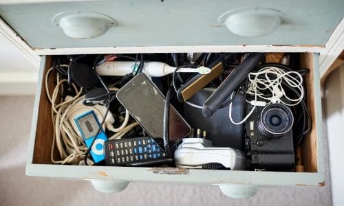 an open drawer on a wooden chest of drawers full with household electrical devices