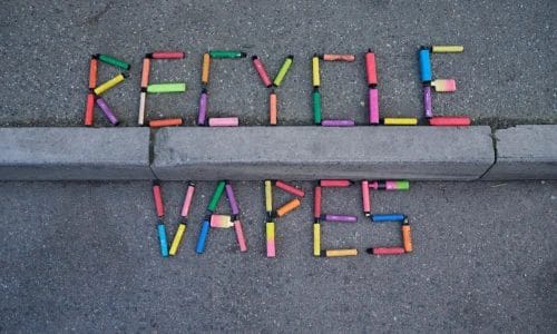 the words "recycle vapes" spelled out on a pavement using old single use vapes