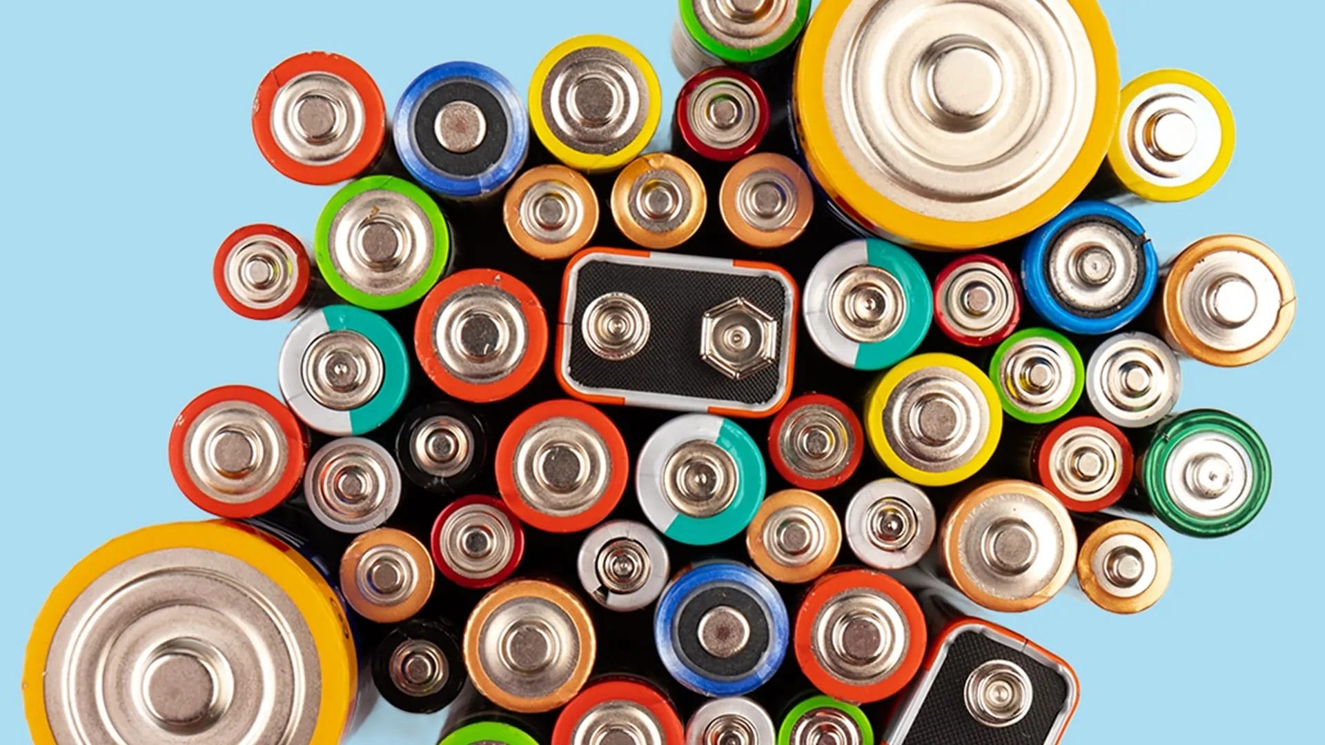 birds eye view of a collection of colourful batteries standing on their ends against a pale blue background