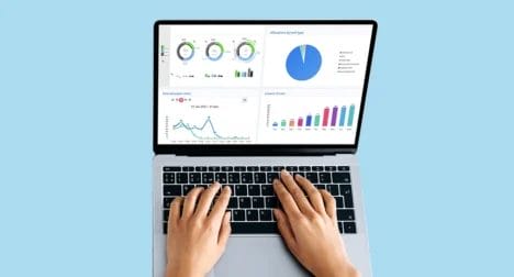 a top shot of an open laptop with various graphs on the screen against a plain blue background