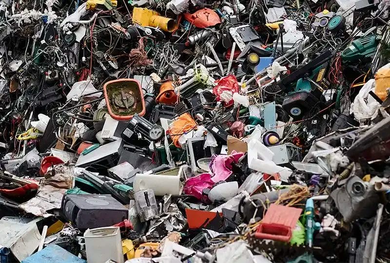 A massive, towering pile of mixed electronic waste at a recycling facility, including tangled wires, plastic casings, and various household appliance
